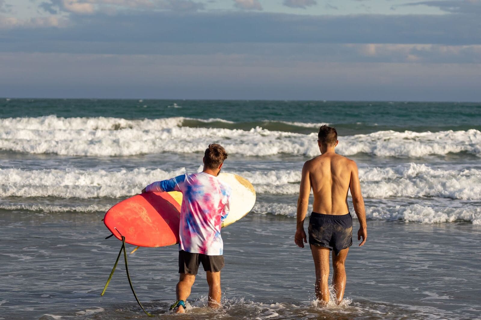 Two surfers carrying their boards to the water on a sunny beach